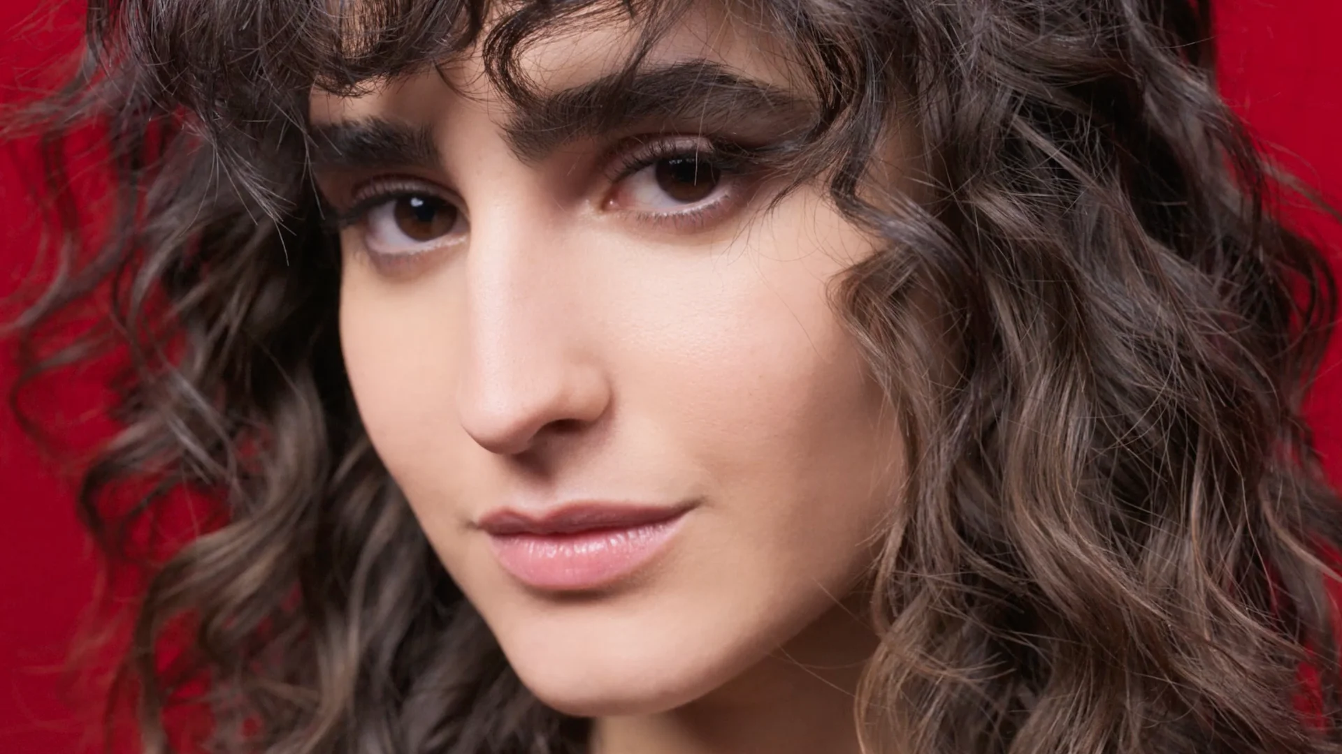 close up of female model's face on red background staring into camera directed by Barnaby Roper